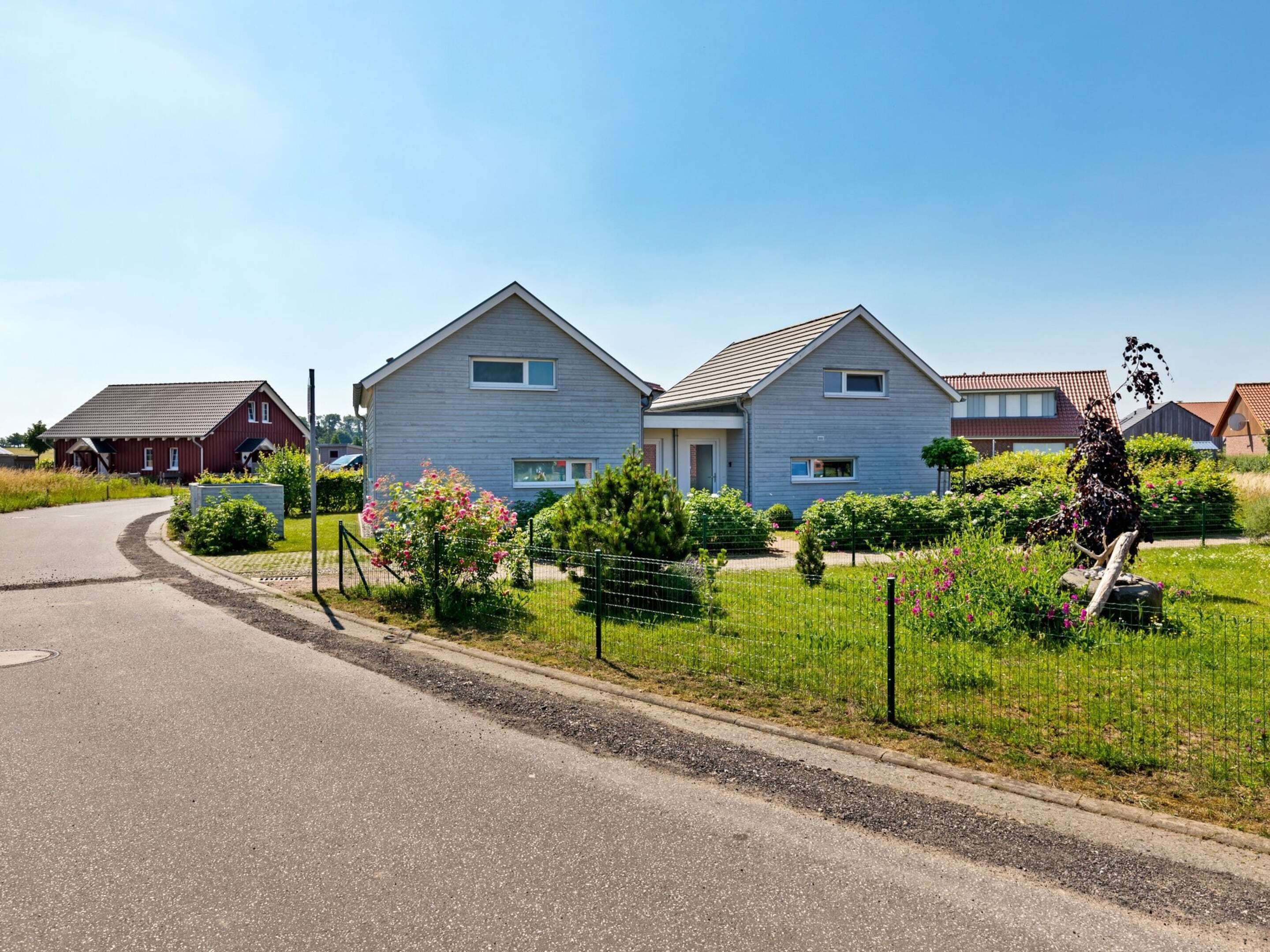Un quartiere residenziale con due case, una strada curva e una zona erbosa con fiori.