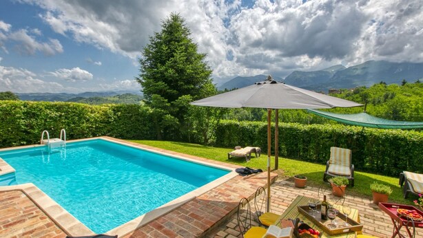 A swimming pool with a view of mountains, a grassy area with a table and chairs, and a large umbrella. - Countryside Villa in Amandola With Swimming Pool (Amandola)