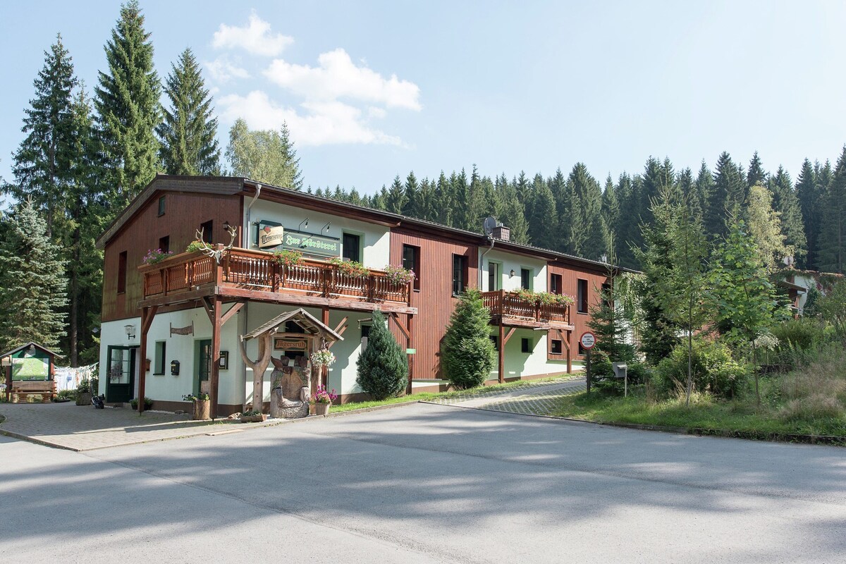 A two-story building with a balcony, a sign for 'Jägerstuben', and a view of a forested area.