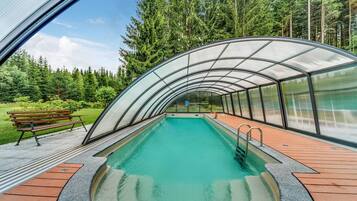 A swimming pool with a glass enclosure, surrounded by a wooden deck and a bench.
