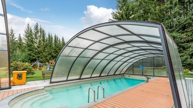 Piscina coberta com deck de madeira e estrutura de vidro.
