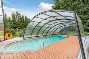 Une piscine couverte dotée d’une terrasse en bois et d’une structure en verre.