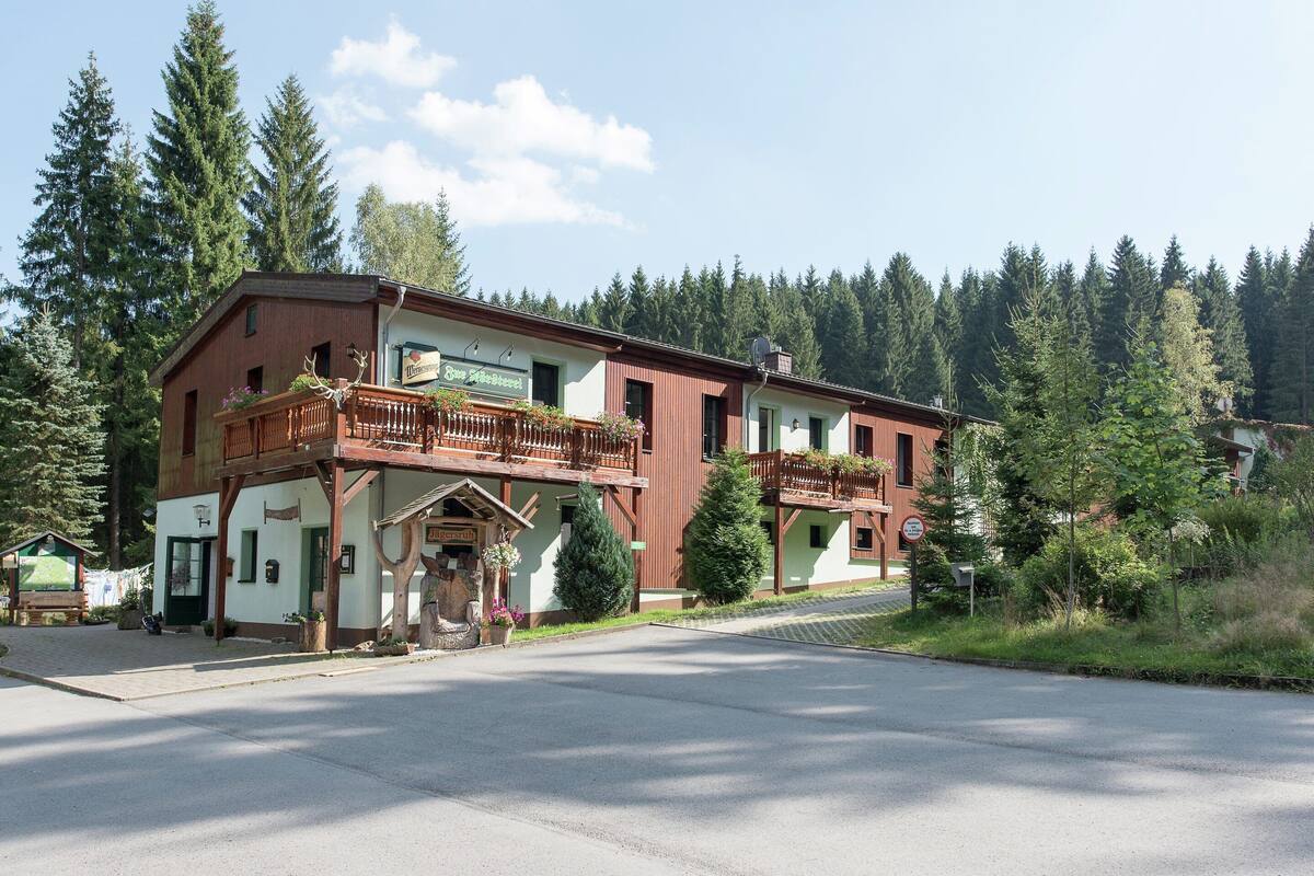 Ein zweistöckiges Gebäude mit Balkon, einem Schild mit der Aufschrift 'Jägerstuben' und Blick auf ein bewaldetes Gebiet.