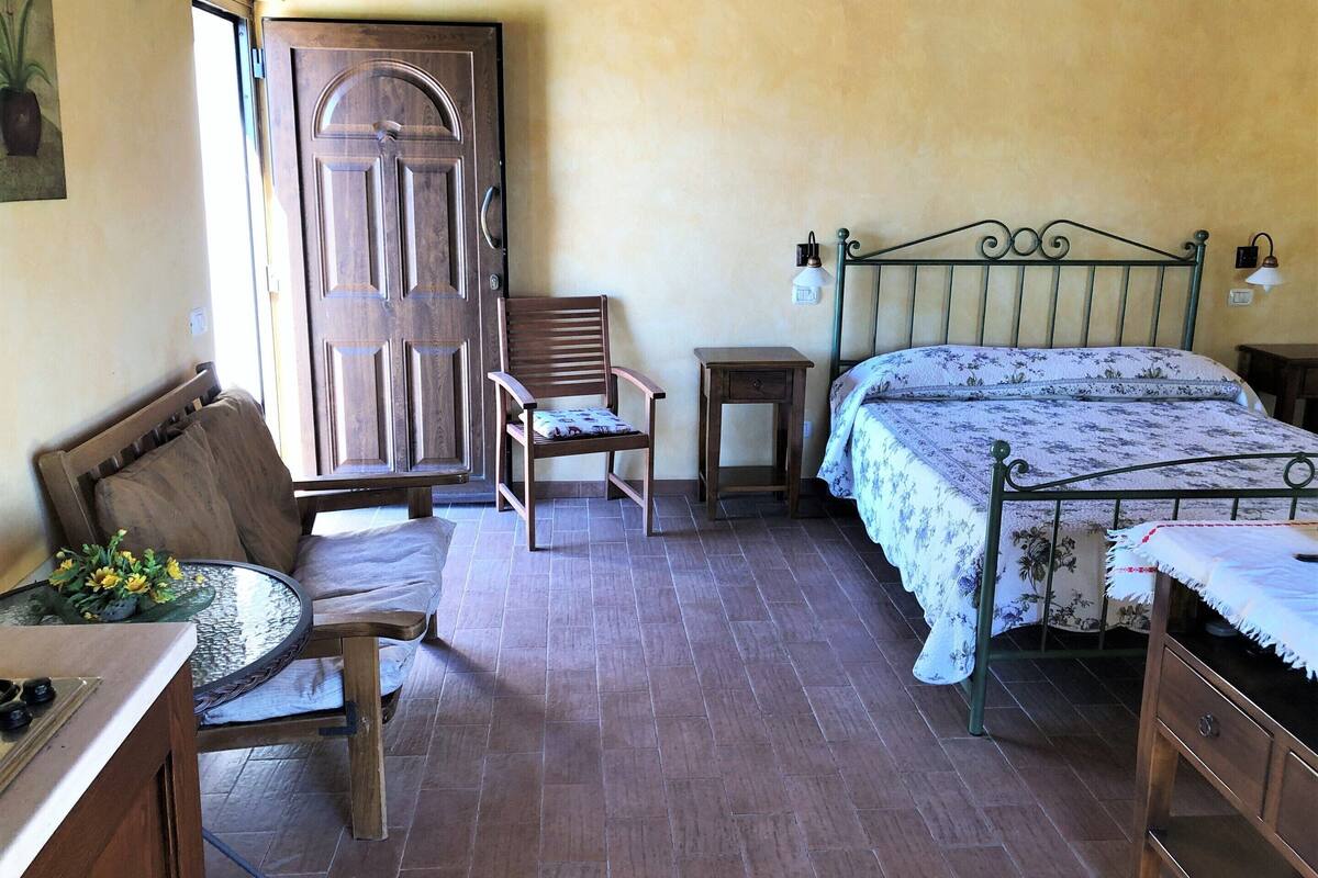 A bedroom with a wooden bed, a chair, a small table, and a door.