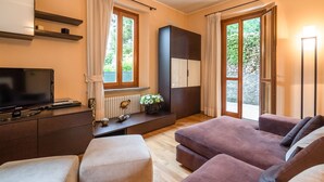 A modern living room with a flat-screen TV, a sofa set, a cabinet, and a window with curtains. - Modern Apartment in Meina Near the Lake (Meina)
