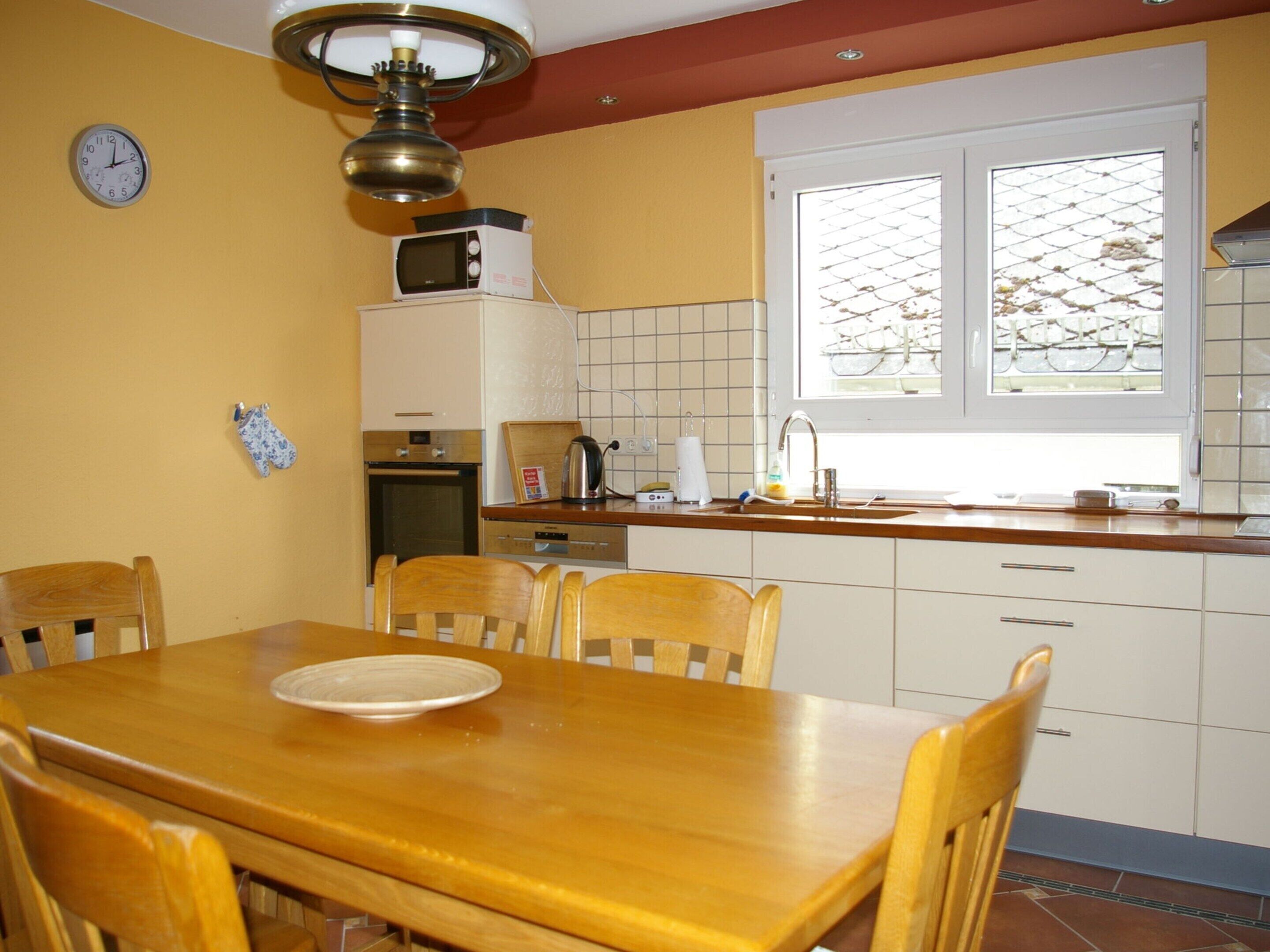 A kitchen with a wooden table and chairs, a microwave, and a window with a view of trees.