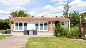 Un bâtiment d’un seul étage, doté d’un toit recouvert de tuiles rouges, de grandes fenêtres et d’un patio aménagé avec des sièges extérieurs.