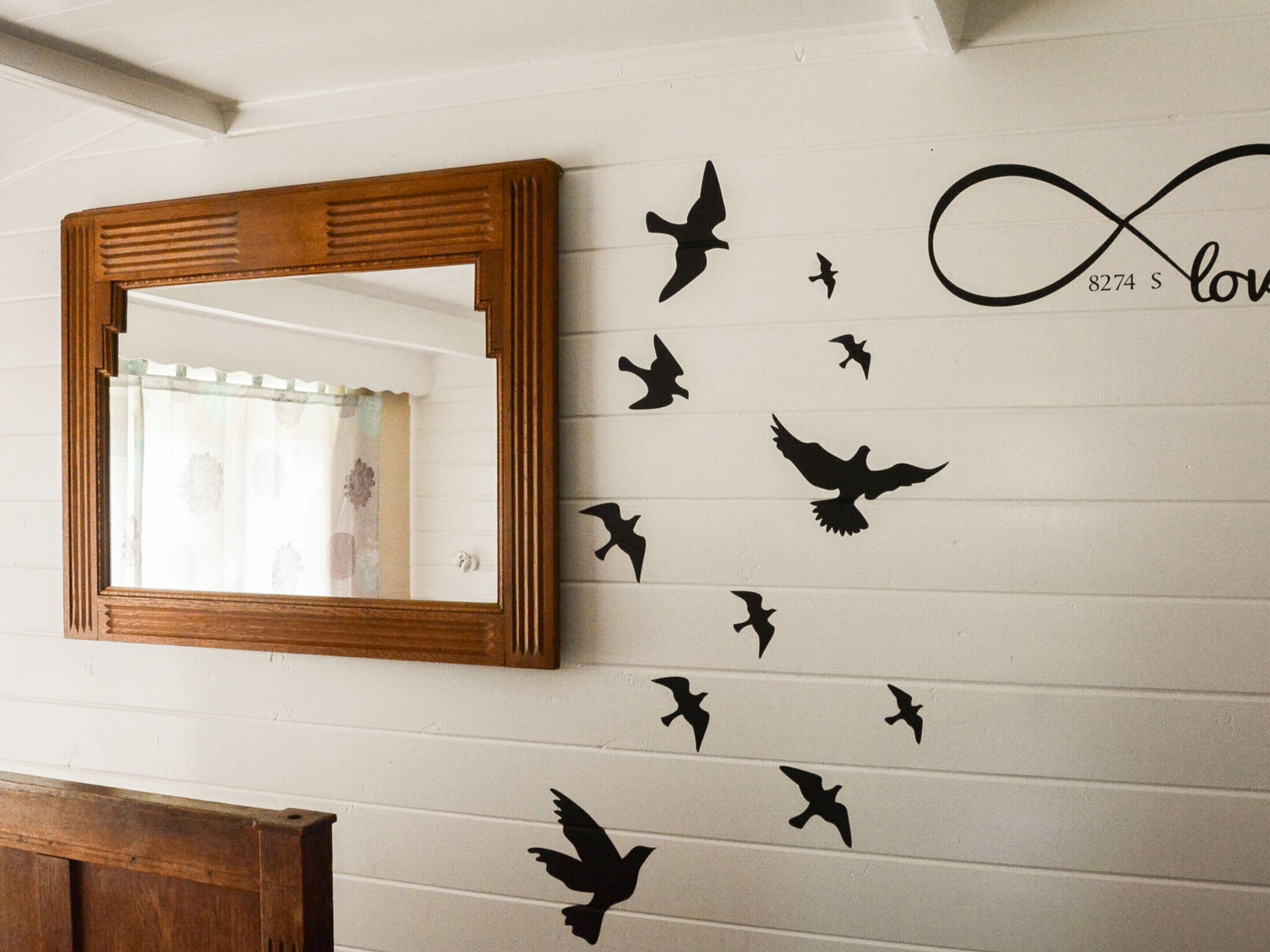 A wall with a mirror and silhouettes of birds flying.