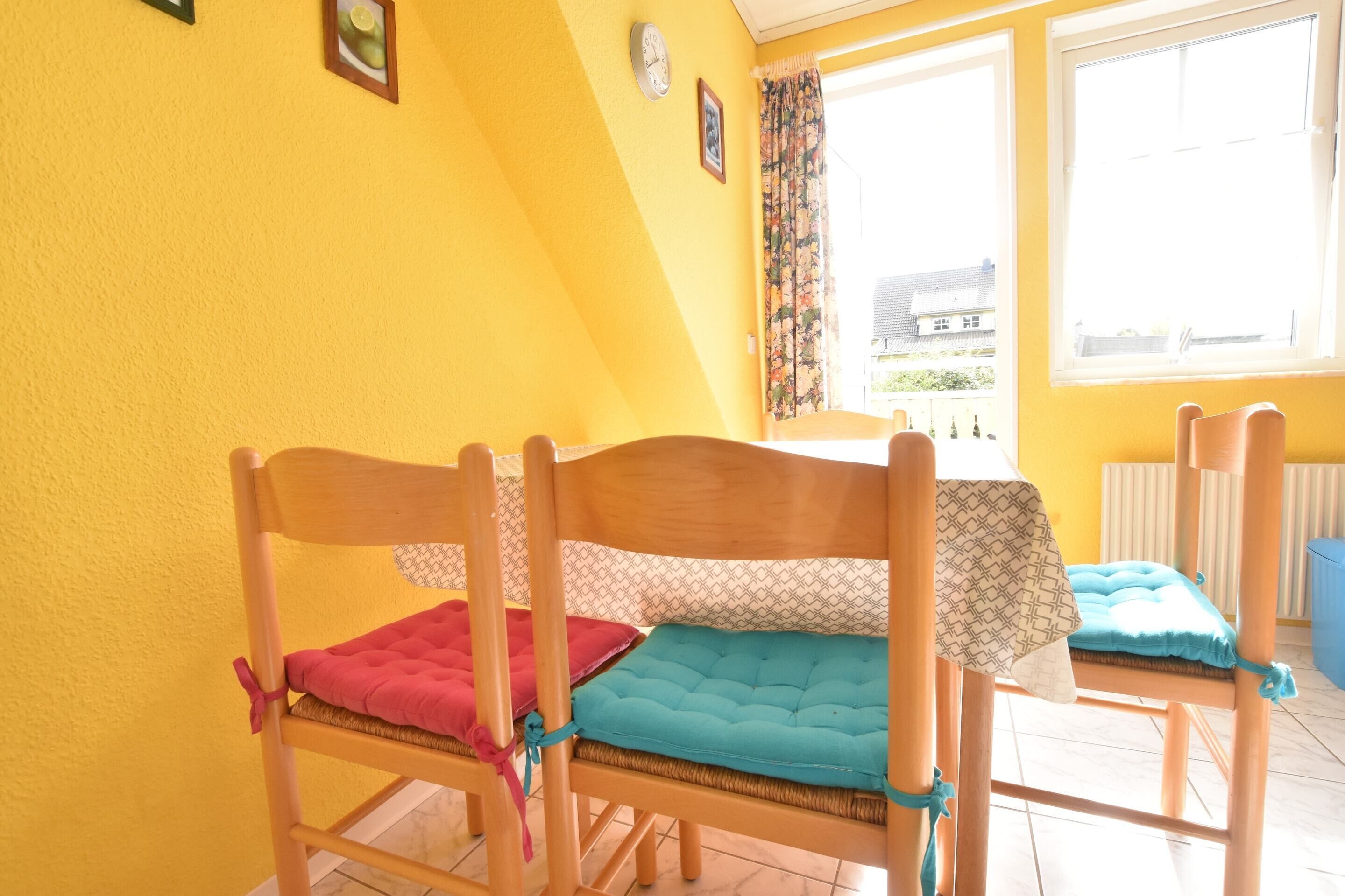 A room with yellow walls, two wooden chairs with cushions, a table, and a window with curtains.