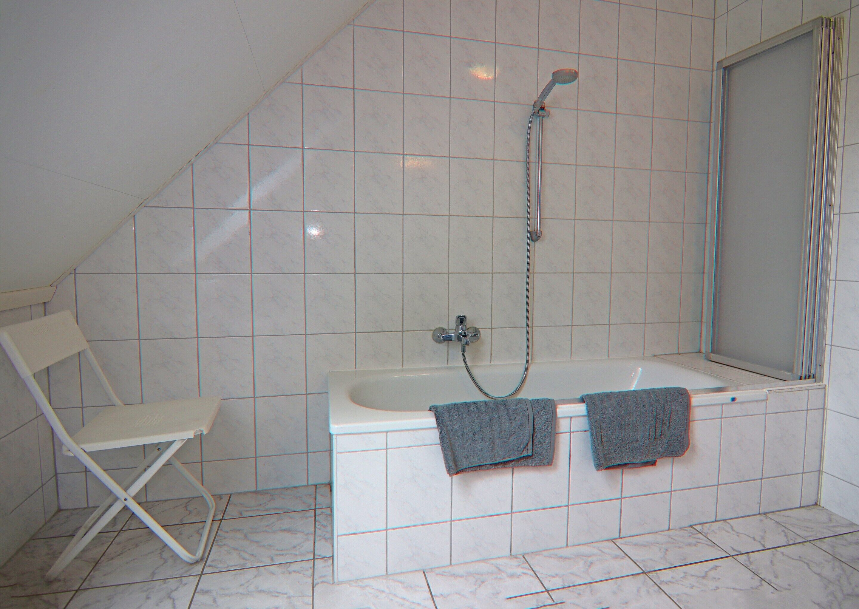A bathroom with a bathtub, a shower, a white chair, and two towels hanging on the wall.