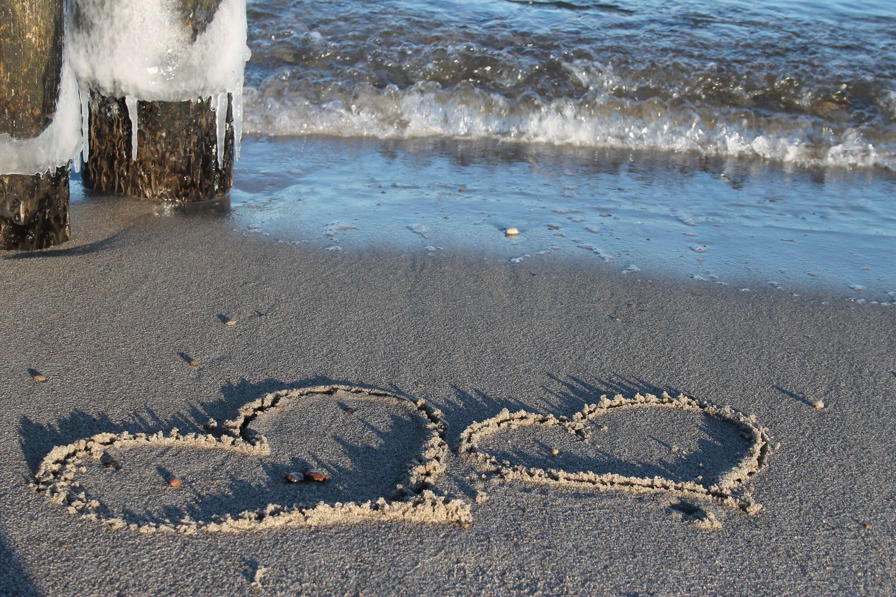 A sandy beach with footprints and a heart drawn in the sand.