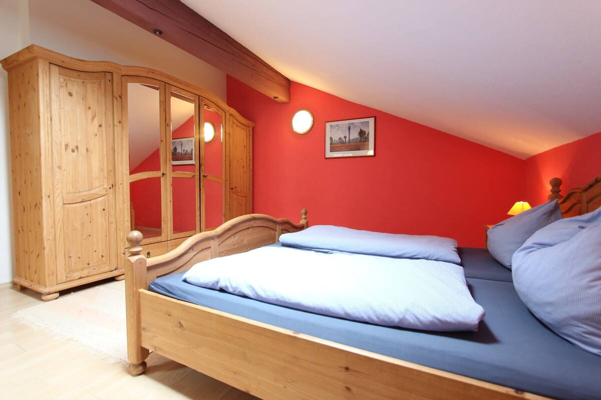 A bedroom with a wooden bed, a wardrobe, and a red wall.