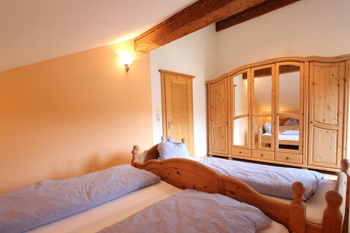 A bedroom with two wooden beds, a wooden wardrobe, and a wall-mounted light fixture.