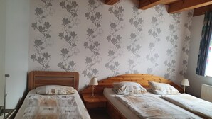 Ein Schlafzimmer mit zwei Betten, Holz-Kopfteilen, einem Nachttisch mit Lampe und blumigem Wandpapier.