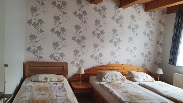A bedroom with two beds, wooden headboards, a nightstand with a lamp, and floral wallpaper. - Large Detached Holiday Home in Hesse With Private Garden and Terrace (Homberg)