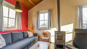 A cozy living room with a sofa, a chair, a table, a fireplace, and large windows with curtains. - Tranquil Holiday Home in Lage Zwaluwe With Terrace (Lage Zwaluwe)