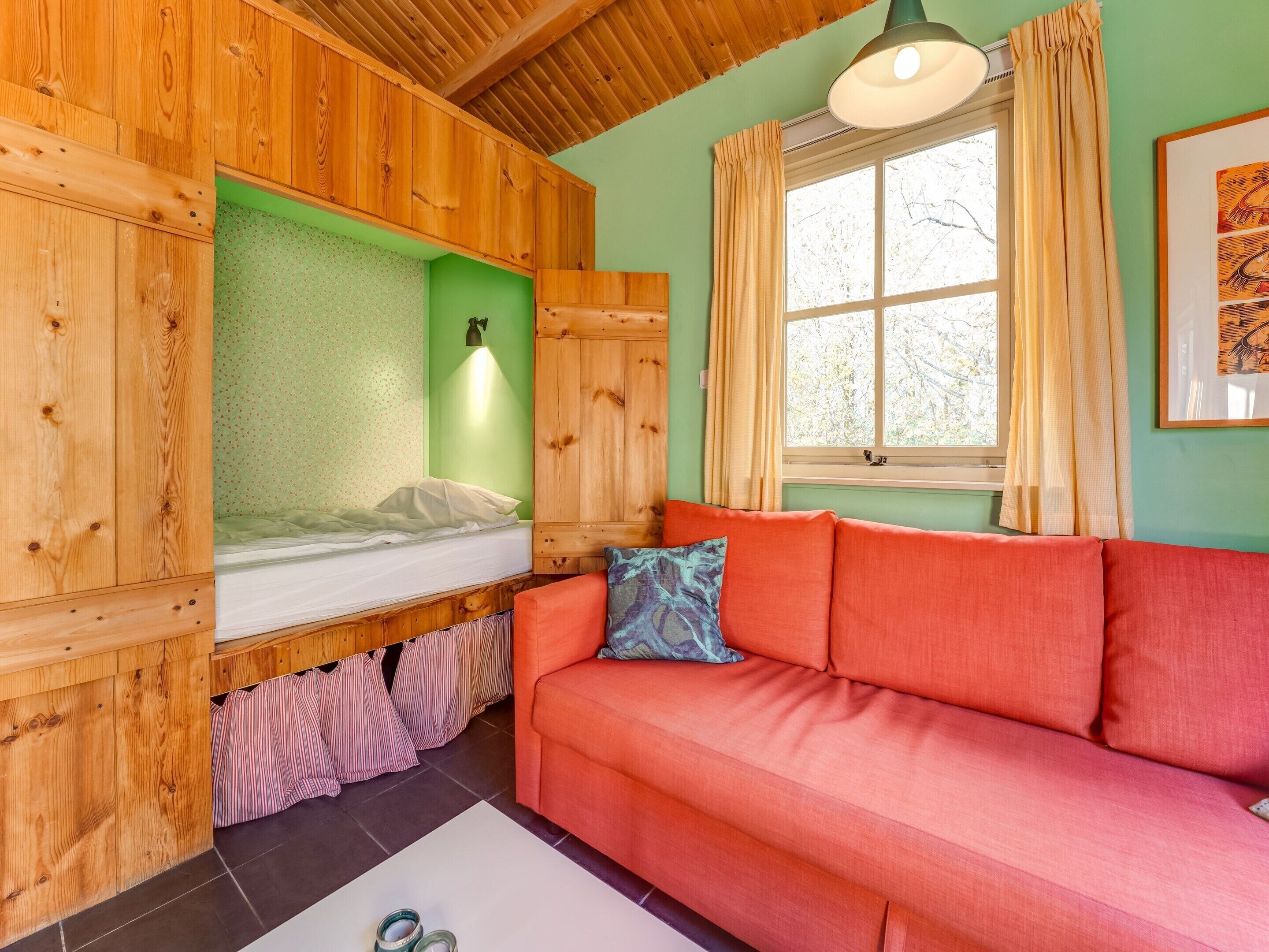 Una habitación acogedora con una cama litera, un sofá rojo y una ventana con cortinas.