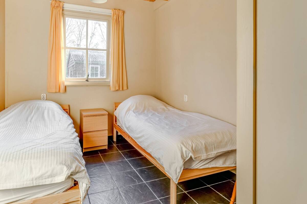 A bedroom with two single beds, a nightstand, a window with curtains, and a ceiling light.