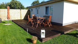 A single-story mobile home with a deck, a dining table with chairs, an umbrella, and a potted plant. - Modernly Furnished Holiday Home Near the Beach (Rostock)