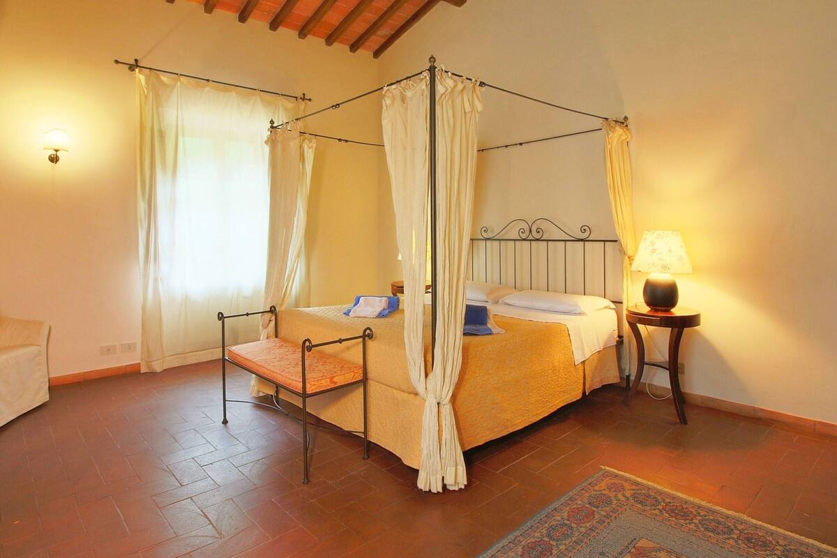 Un lit à baldaquin à quatre poteaux avec une tête de lit en bois, une table de chevet avec une lampe et un tapis à motifs sur le sol.