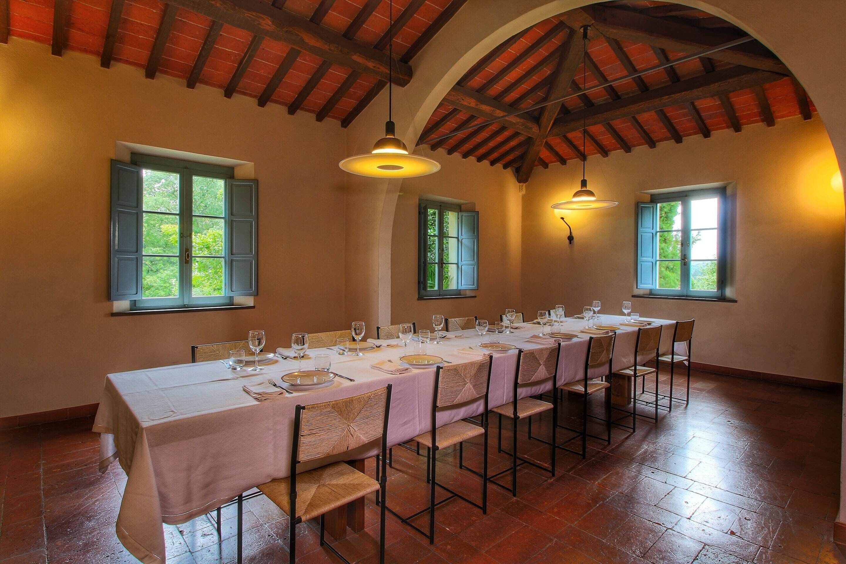 Ein Esszimmer mit einem langen Tisch, der für eine Mahlzeit gedeckt ist, Holzbalken an der Decke und Fenstern mit Fensterläden.