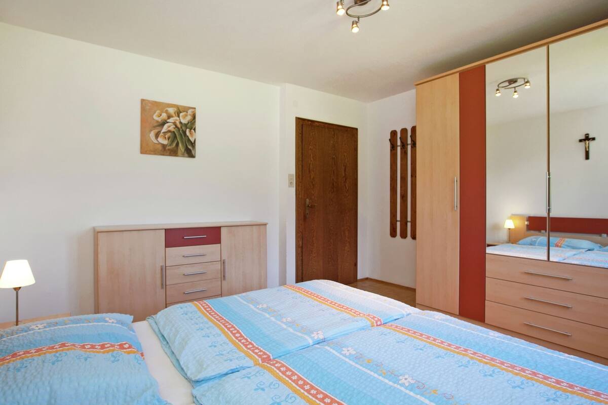 A bedroom with two beds, a wardrobe, a mirror, and a painting on the wall.