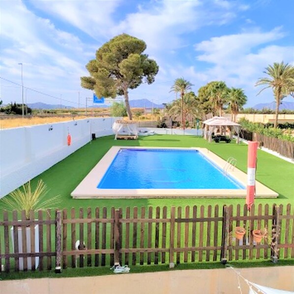 Ein rechteckiger Pool mit Holzzaun im Vordergrund, umgeben von Grünpflanzen und Palmen.