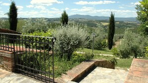 A garden with a stone bench, a metal fence, and a view of distant hills. - Farmhouse With air Conditioning, Private Terrace and Pool (Citta della Pieve)