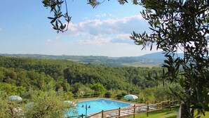 A pool with a wooden deck and lounge chairs, surrounded by lush greenery and a view of distant hills. - Farmhouse With air Conditioning, Private Terrace and Pool (Citta della Pieve)