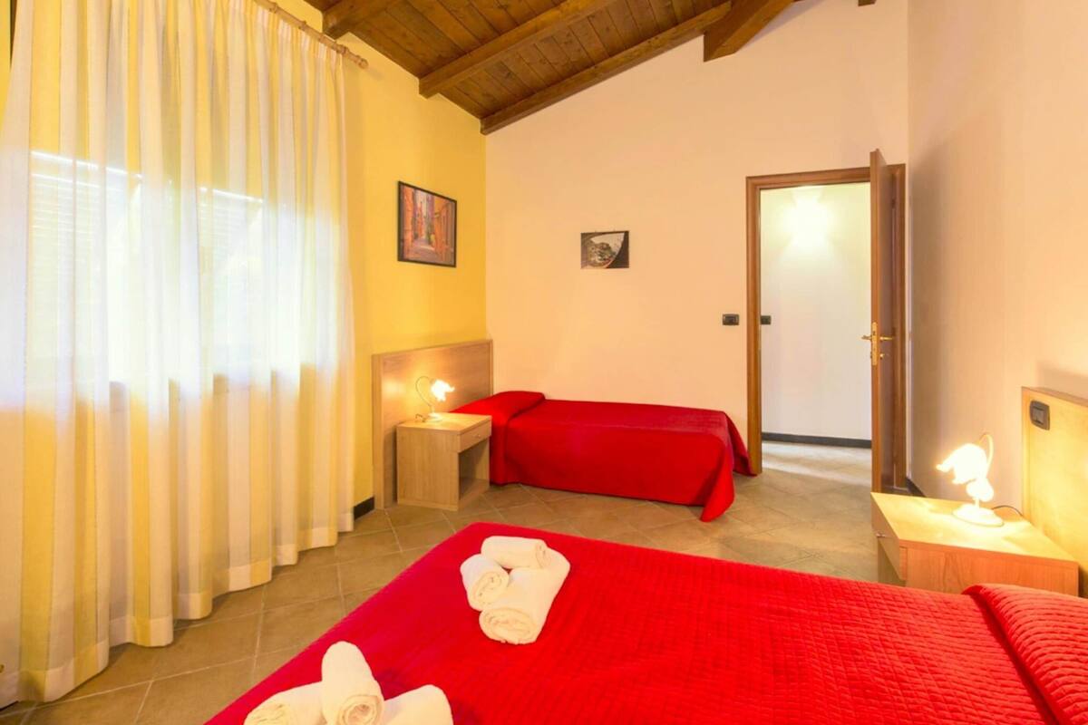 A hotel room with two beds, a wooden ceiling, a door, and a window with curtains.