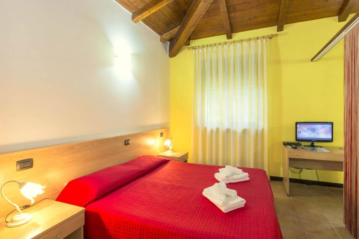 A hotel room with a bed, bedside lamps, a desk with a computer, and a window with curtains.