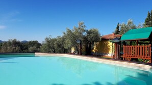 A clear blue swimming pool with a wooden deck and a green canopy structure. - Charming Residence in the Hills Surrounding La Spezia (Bolano)