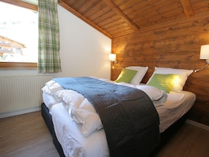 A bedroom with a wooden ceiling, a bed with white bedding and green pillows, a window with a green curtain, and a wall-mounted light fixture. - Private Chalet in Grossarl With Sauna and Beautiful View (Grossarl)