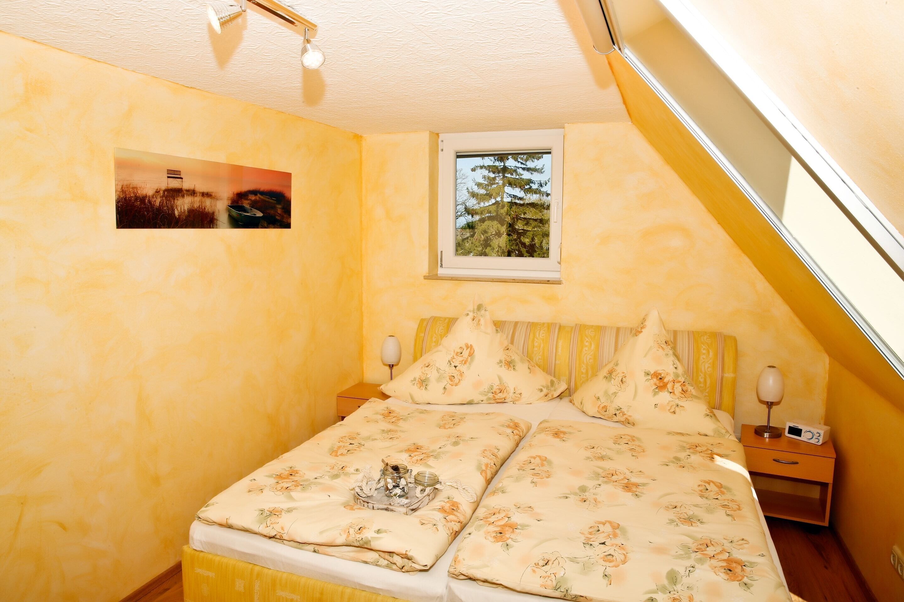 A bedroom with a bed, two bedside tables, a window, and a picture on the wall.