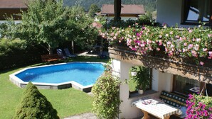 Una piscina rodeada de vegetación, un patio con mesa y sillas, y vistas a montañas al fondo.