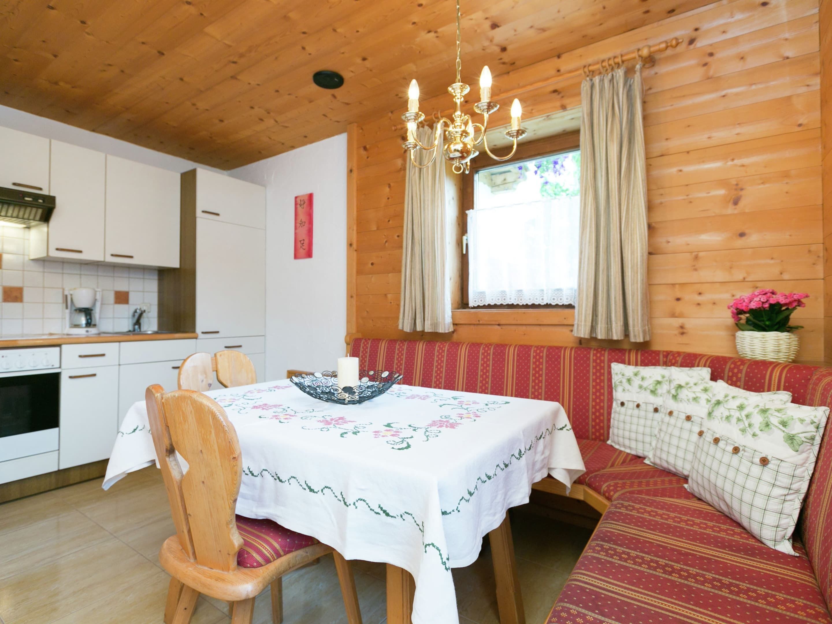 A cozy cabin-style room with a wooden interior, a dining table with chairs, a bench with cushions, and a window with curtains.