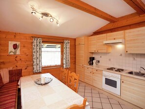 A cozy wooden cabin with a dining area, a kitchen with a stove and sink, and a window with curtains. - Alluring Apartment With Swimming Pool in Waidring Tyrol (Waidring)