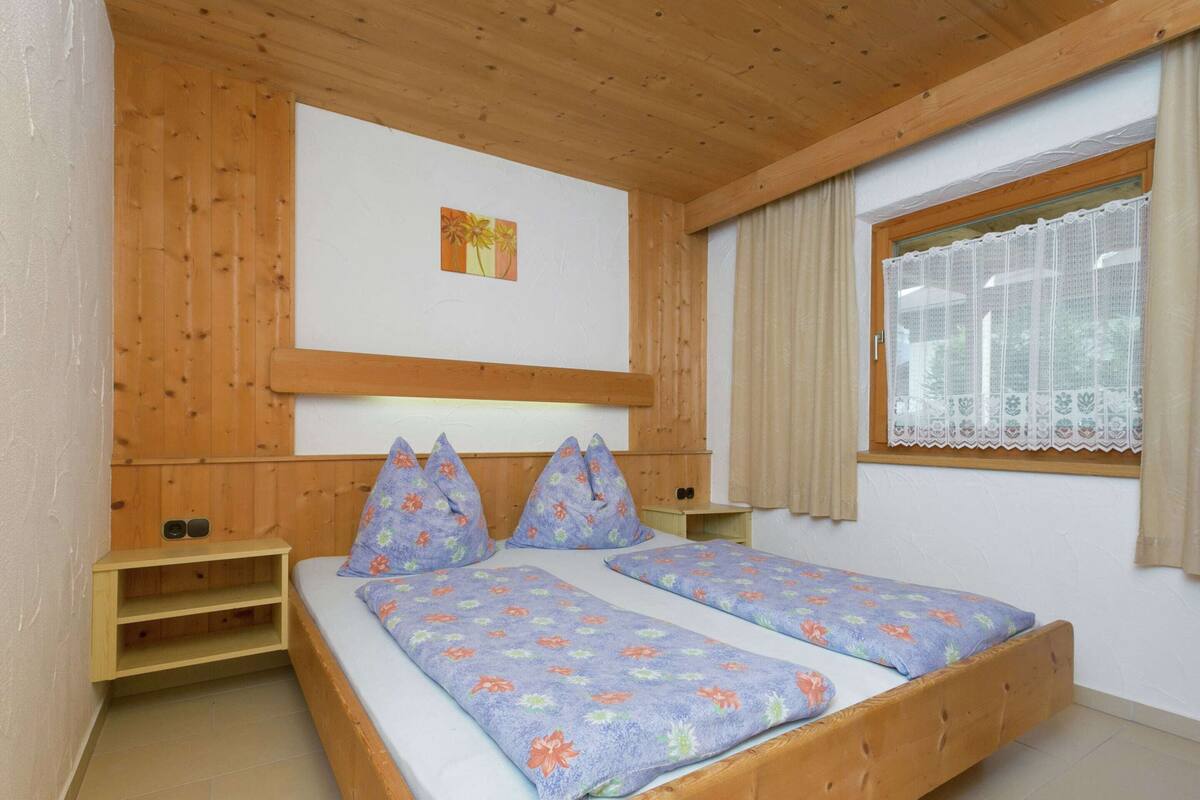 Parivuode, jossa on kukallinen vuodevaatesetti, puinen pääty ja pieni yöpöytä.