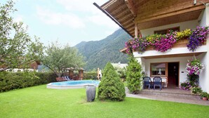 Una casa con balcón de madera, piscina y césped bien cuidado.