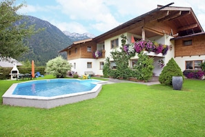 Eine zweistöckige Chalet mit Pool, umgeben von üppiger Vegetation und Bergen im Hintergrund.