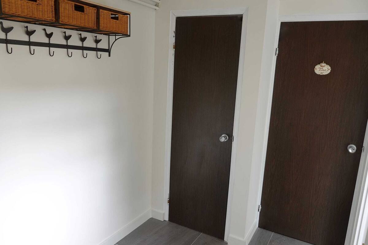 Ein Flur mit zwei dunklen Holztüren, einer weißen Wand und einem Regal mit Körben und Haken.