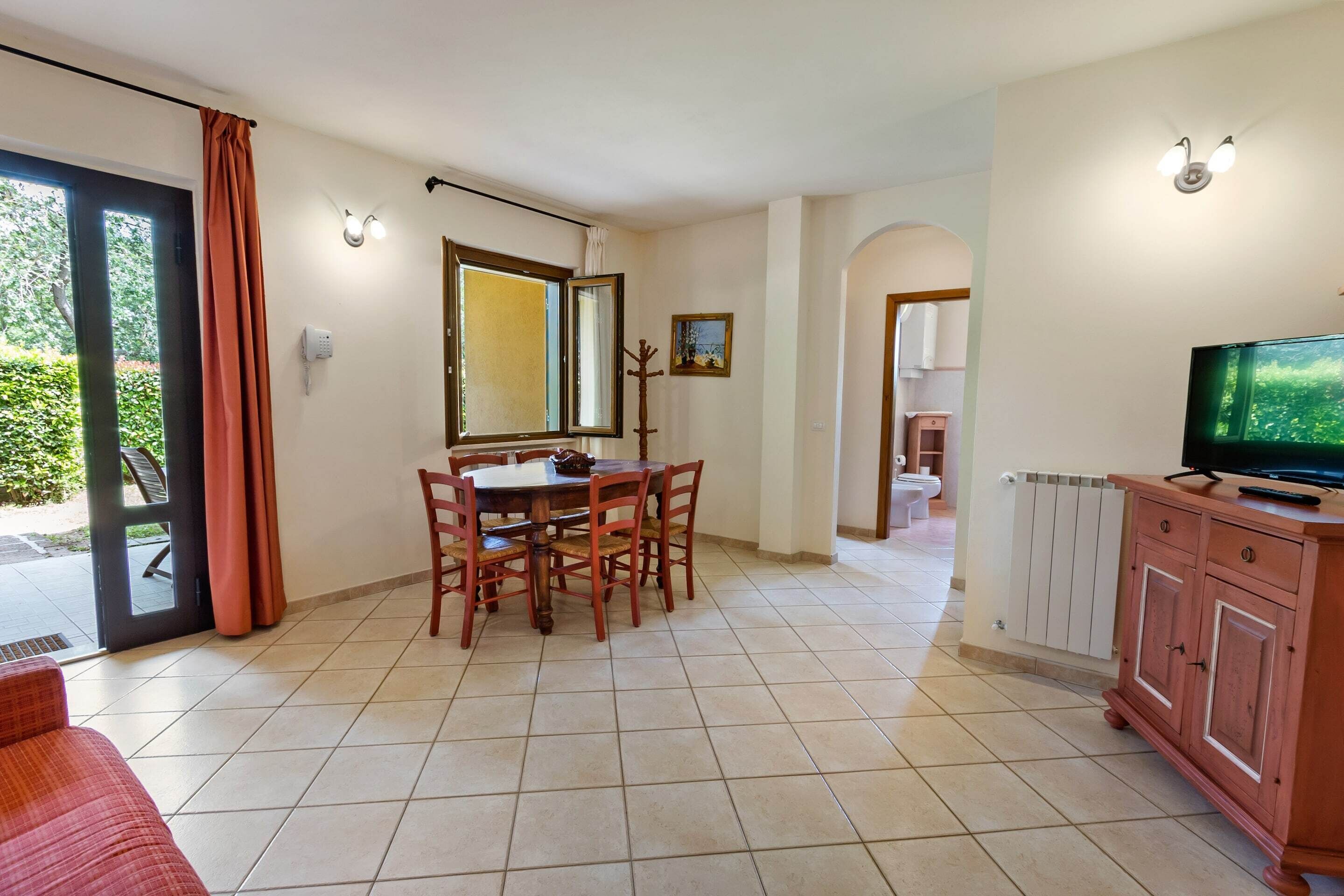 Un coin repas avec une table et des chaises, un téléviseur posé sur un meuble, et une porte-fenêtre coulissante donnant sur un espace extérieur.