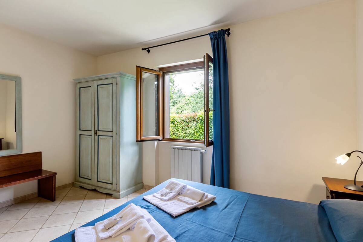 Une chambre à coucher comprenant un lit, une armoire, une fenêtre avec des rideaux, une lampe de chevet et un radiateur.