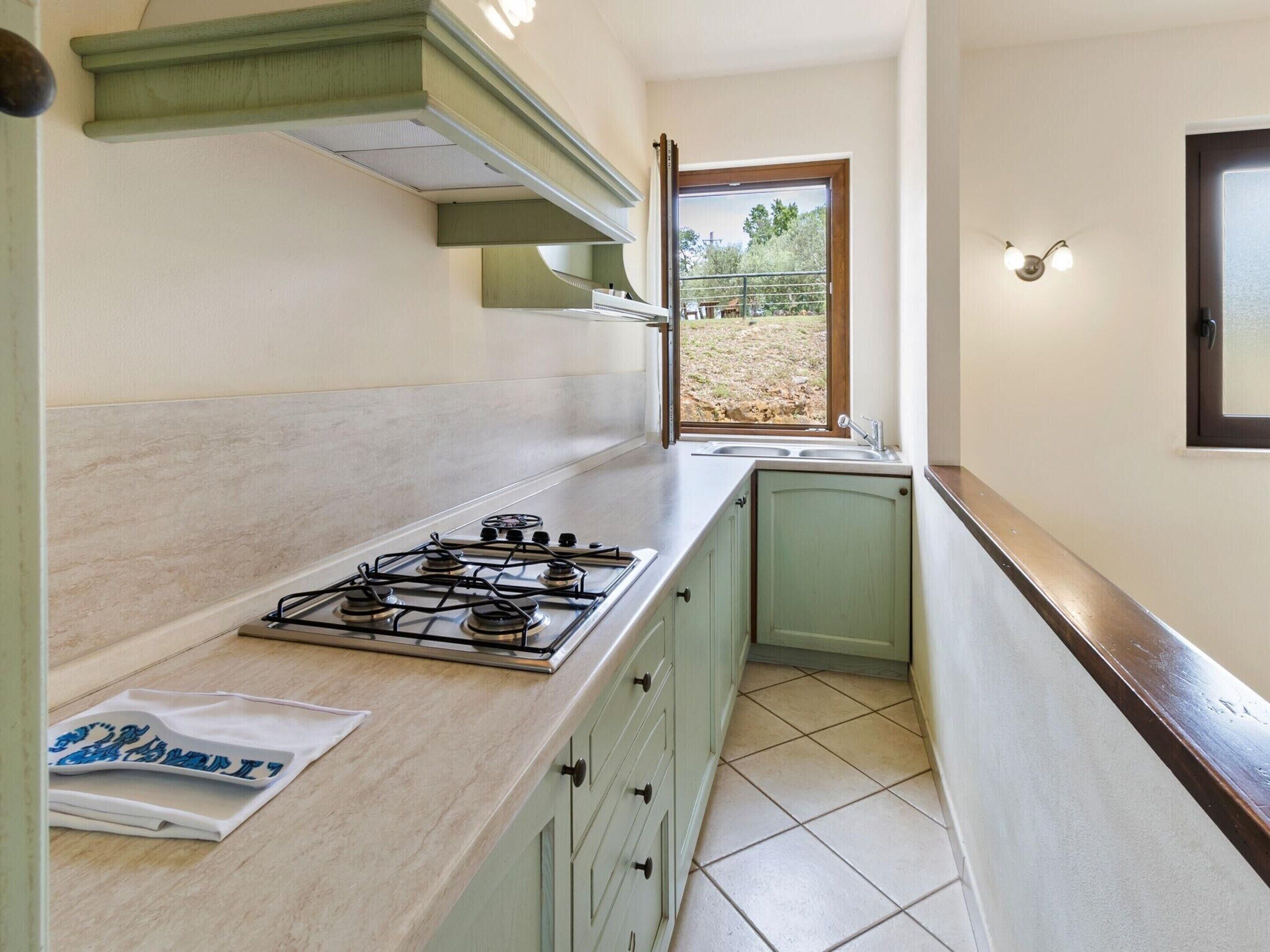 Une cuisine de taille réduite, équipée d’une cuisinière à gaz, d’une fenêtre donnant sur l’extérieur et d’un évier.
