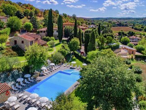 Una piscina con sillas de descanso y sombrillas, rodeada de vegetación y edificios.