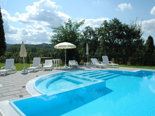 A swimming pool with white lounge chairs and umbrellas, surrounded by trees and a view of hills. - Air-conditioned Flat With Pool and Wellness Area (Citta della Pieve)