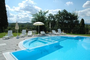 A swimming pool with white lounge chairs and umbrellas, surrounded by greenery and trees. - Air-conditioned Flat With Pool and Wellness Area (Citta della Pieve)