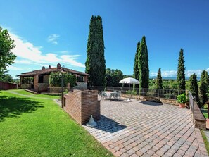 A patio with a brick floor, outdoor furniture, and tall cypress trees. - Air-conditioned Flat With Pool and Wellness Area (Citta della Pieve)