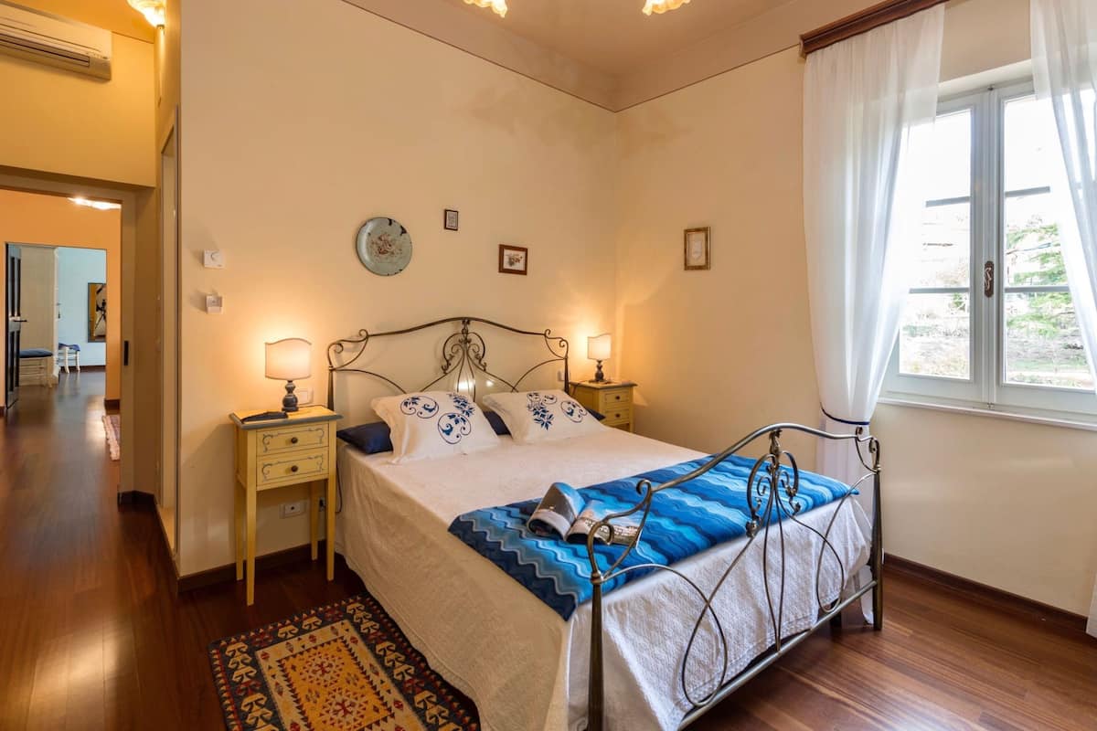 A bedroom with a bed, bedside tables, a lamp, a clock, and a window with curtains.