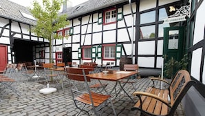 An outdoor seating area with tables and chairs, a building with a sign reading "Restaurant," and a cobblestone floor.